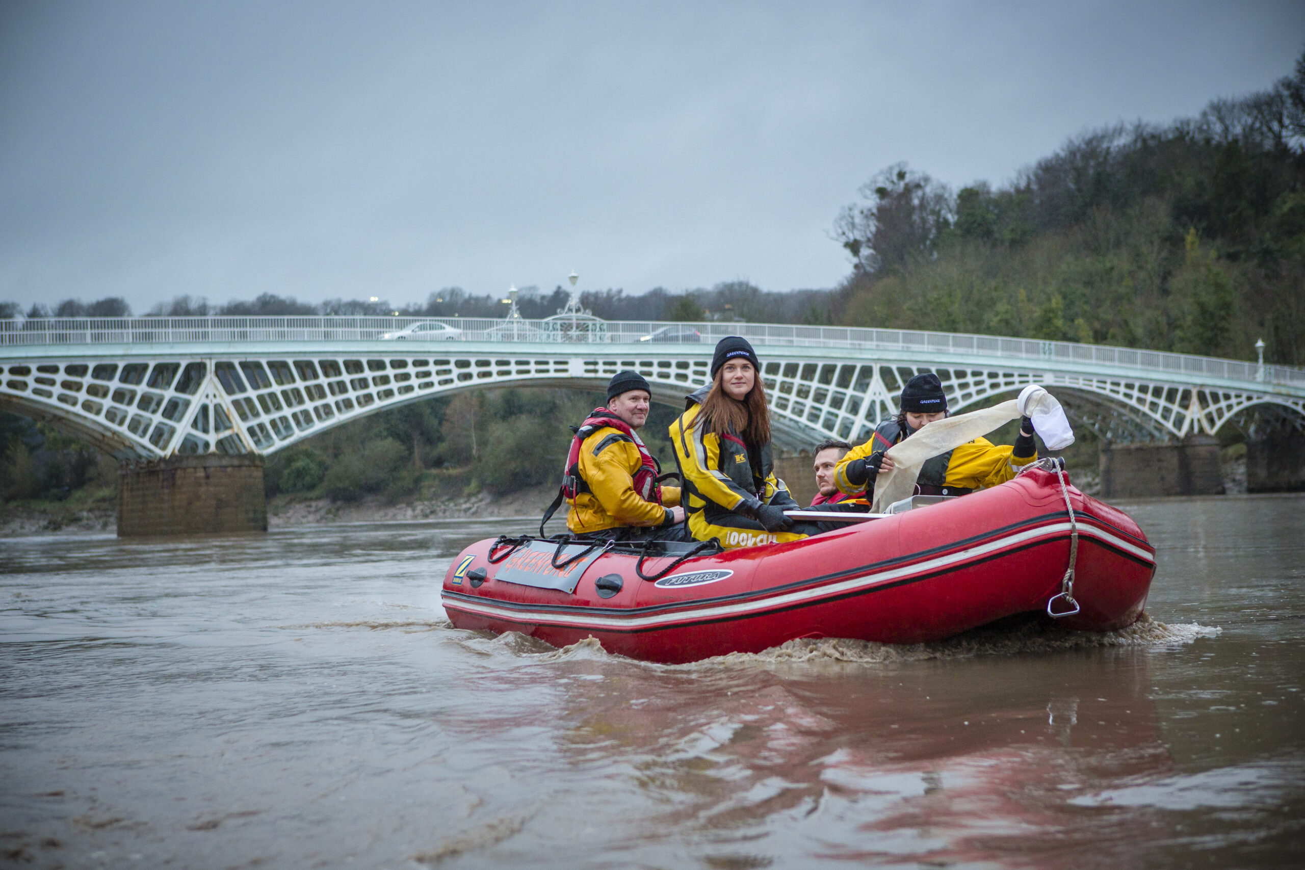 Activists in yellow overalls look downstream as they pilot an inflatable boat along a river.