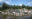 A pile of plastic waste sits next to a lake or river, with palm trees in the background.