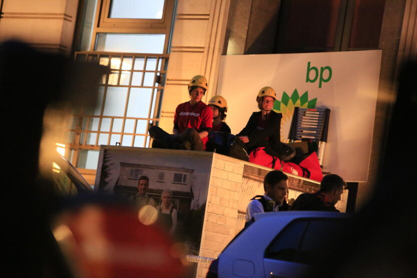 Three people sit on top of a box outside BP headquarters in London.