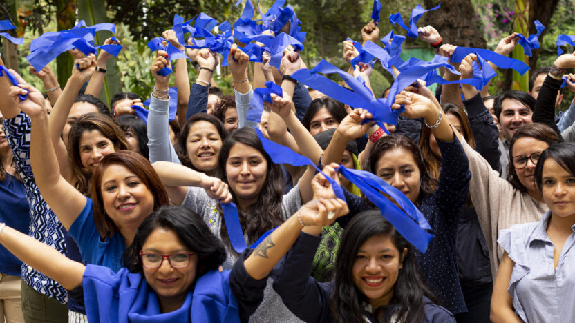 A crowd of people hold up pieces of blue fabric as they smile into the camera.
