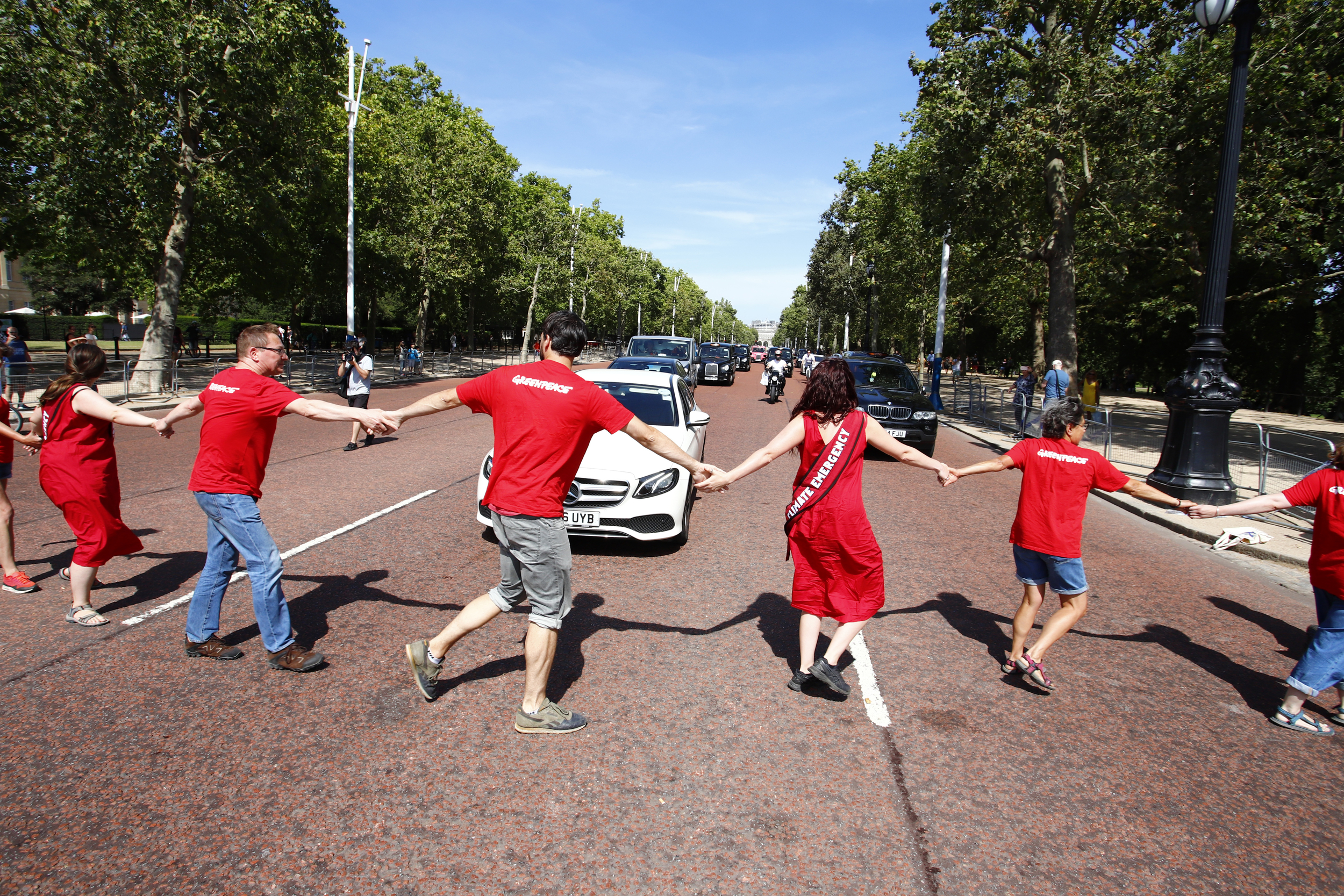 Protesters in red hold hands and dance across a road to block traffic and declare a climate emergency