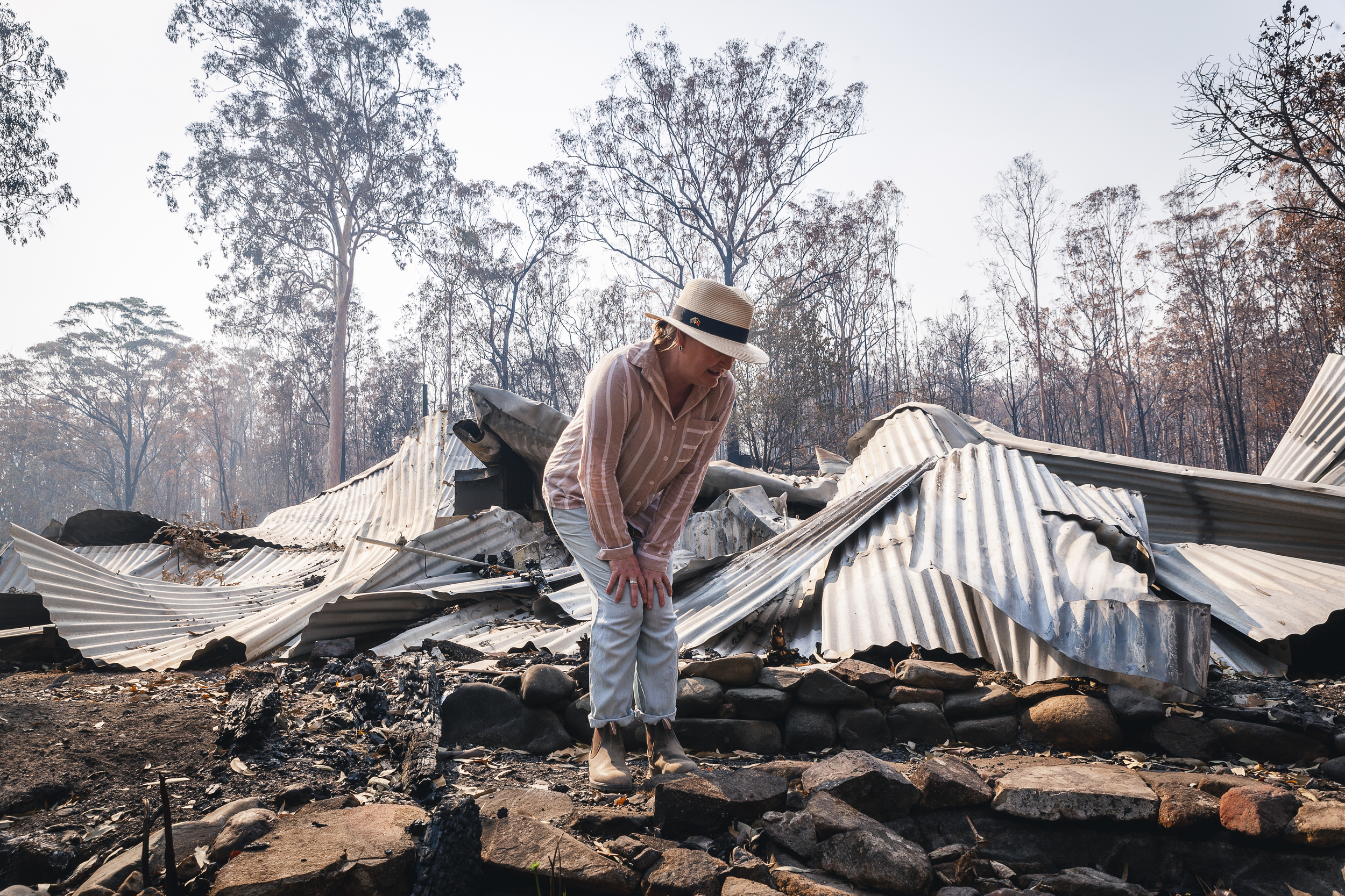 A woman examines the singed ground and remnants of her house which lays collapsed behind her