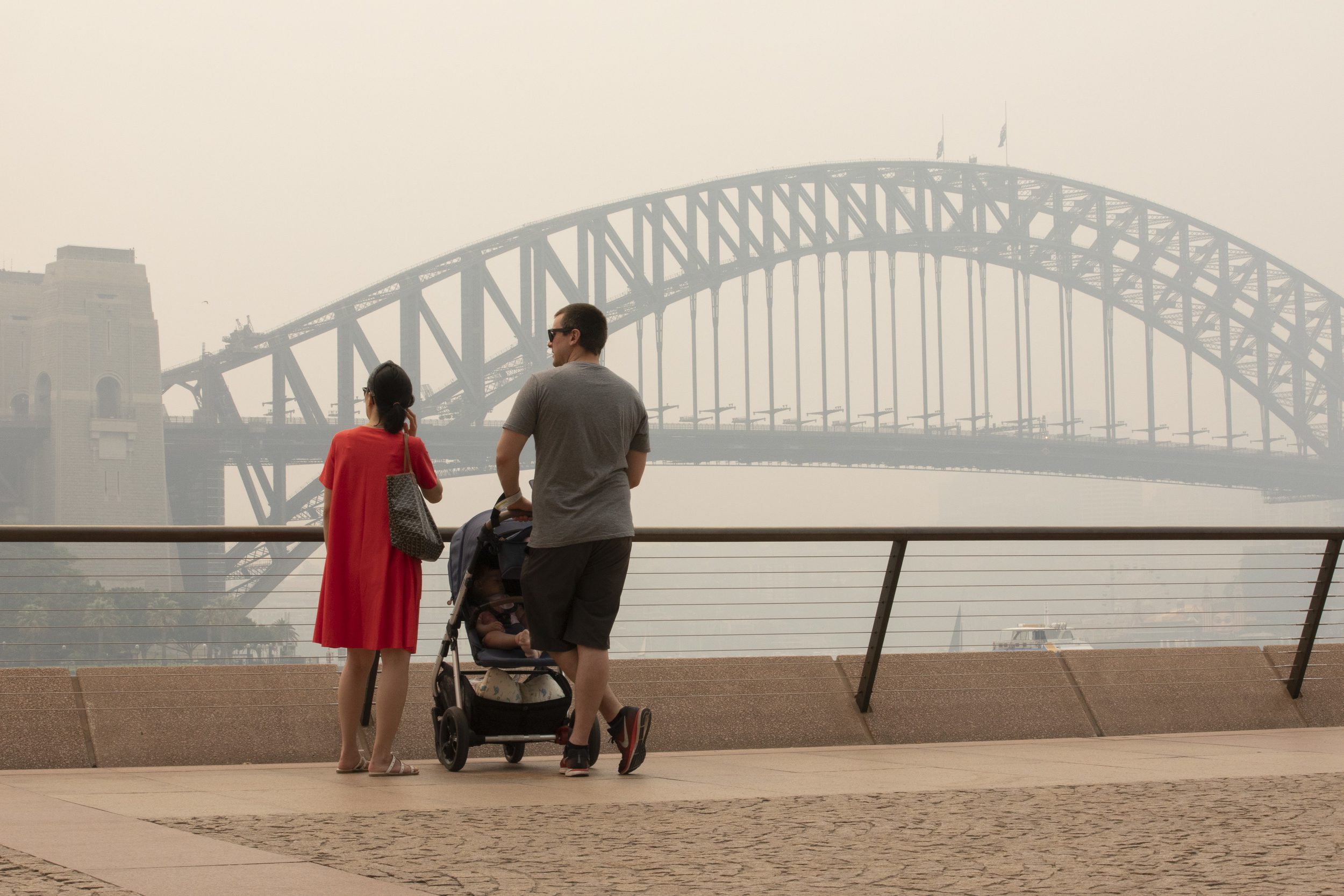 A couple with a pram look over a haze-filled Sydney harbour with the iconic Sydney Harbour Bridge just visible.