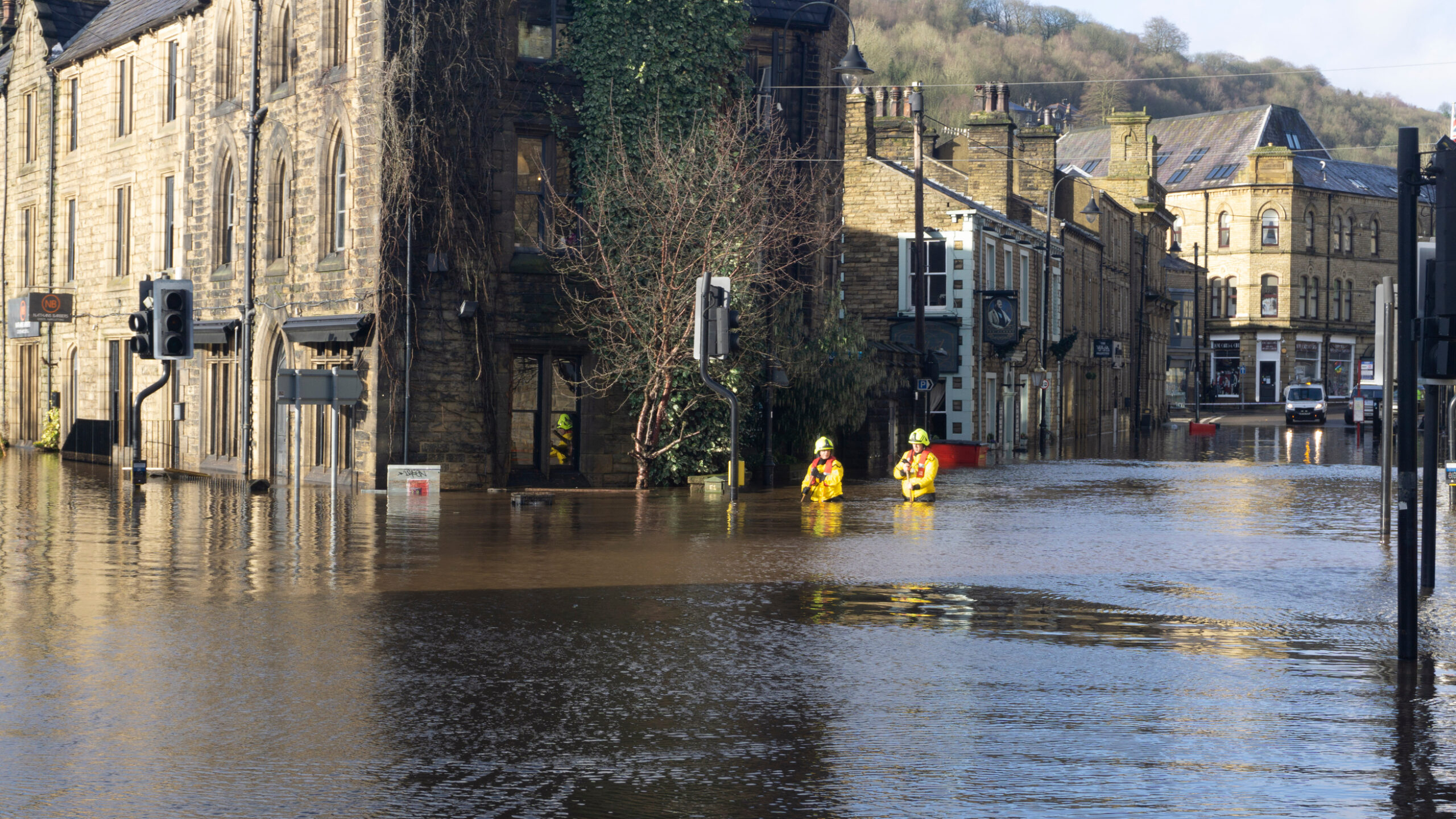 Rescue workers wade through a flooded street lined with old stone houses