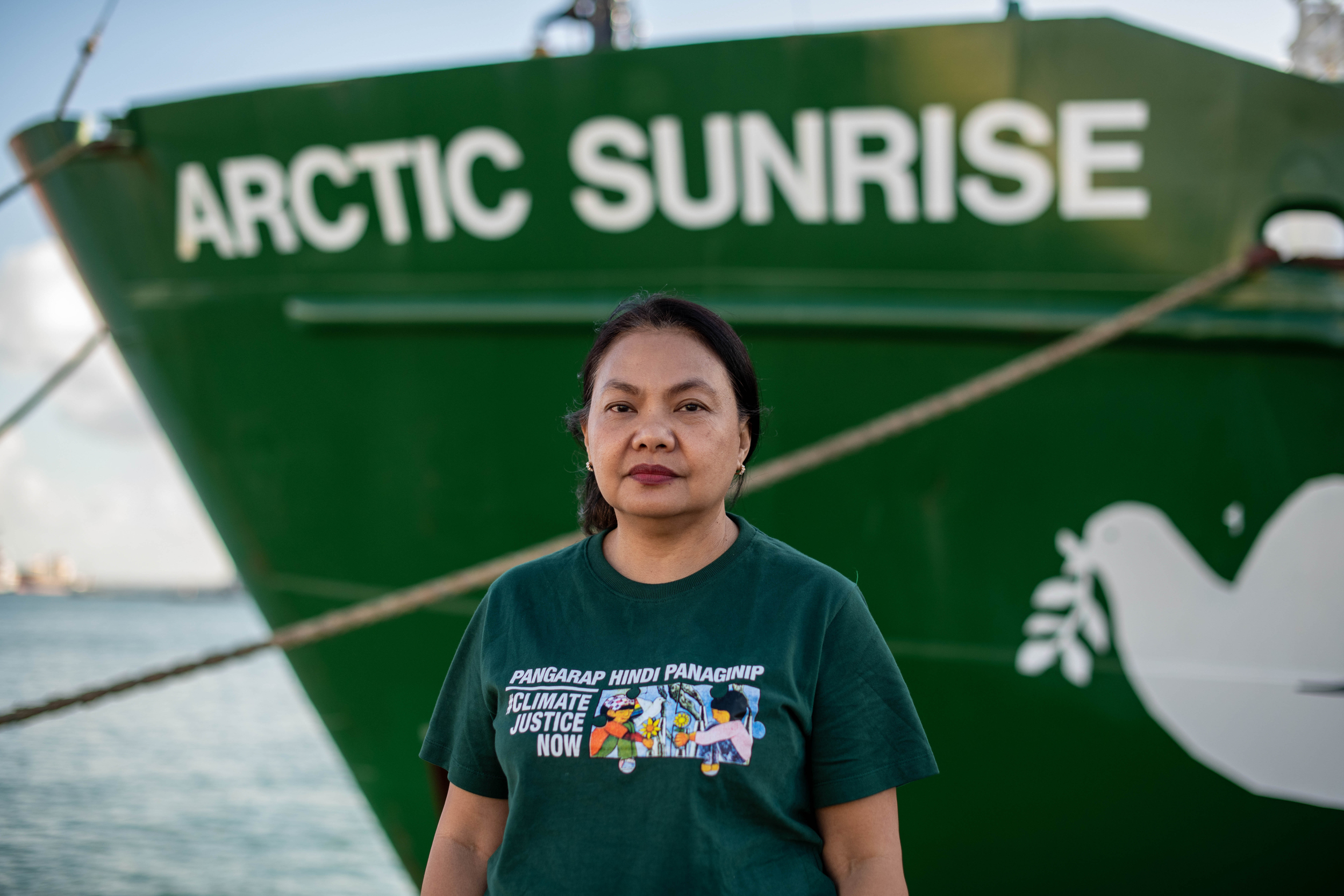 Virginia looks into the camera with a serious expression. She wears a tshirt with a climate justice slogan.