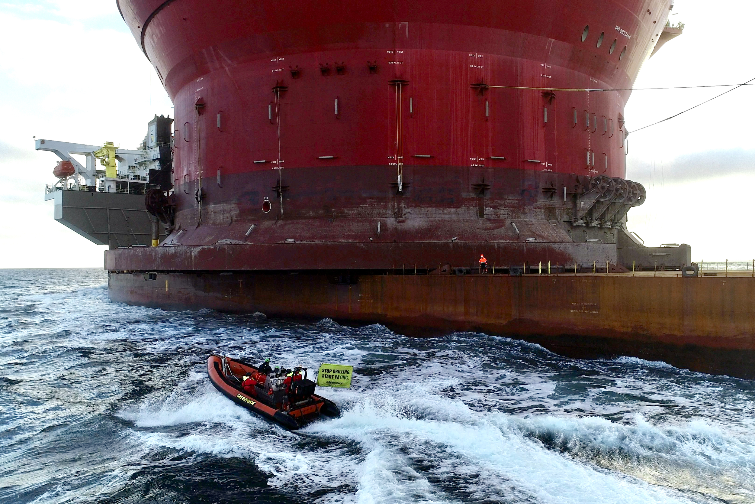A small Greenpeace boat approaching a giant oil platform.