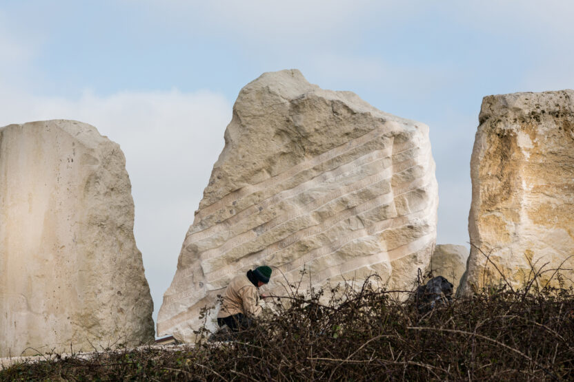 monolithic, cream-coloured stone with carved words amongst other stones on a sunny day.
