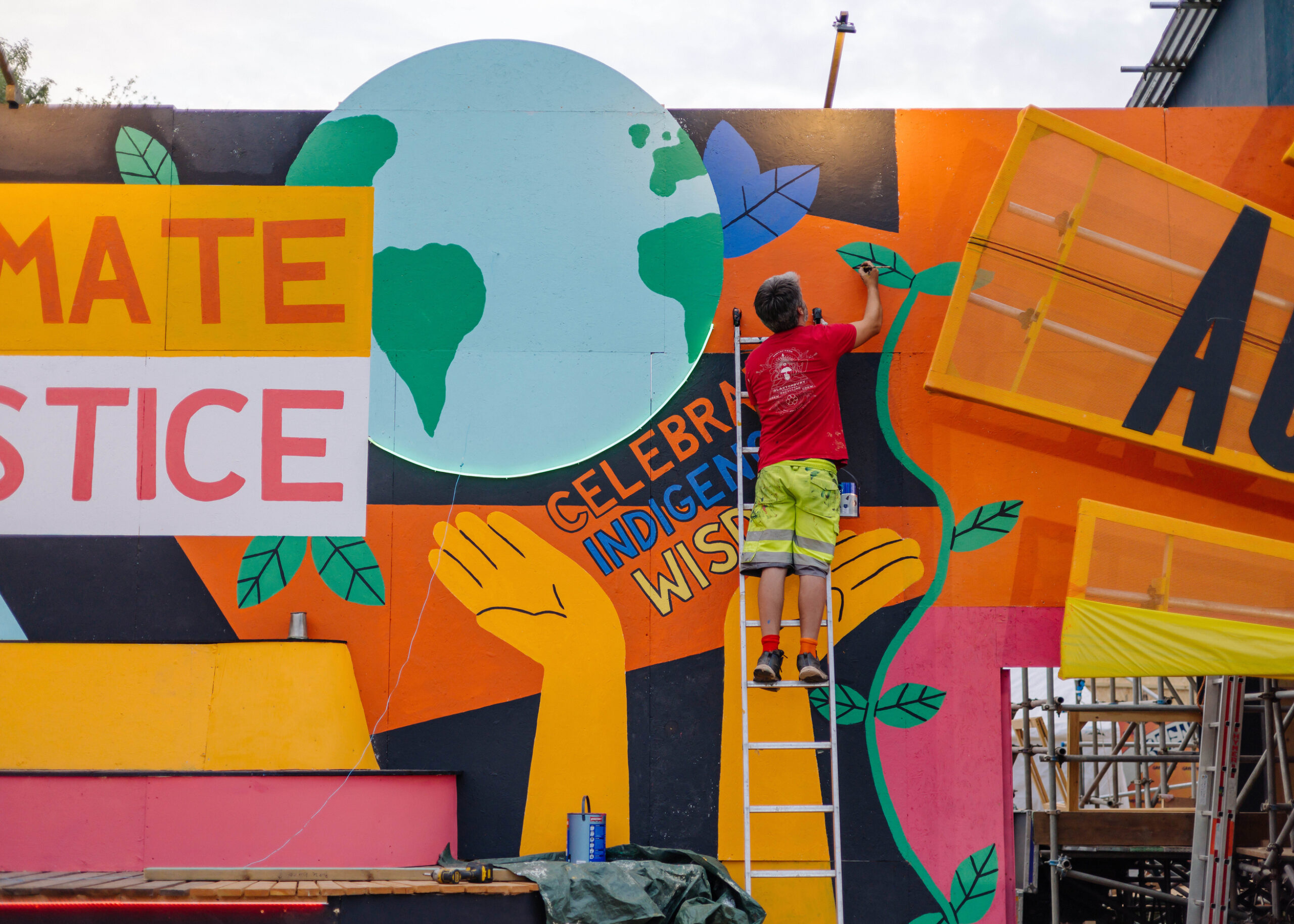 A crew member paints part of a huge colourful mural in the Greenpeace field at Glastonbury.