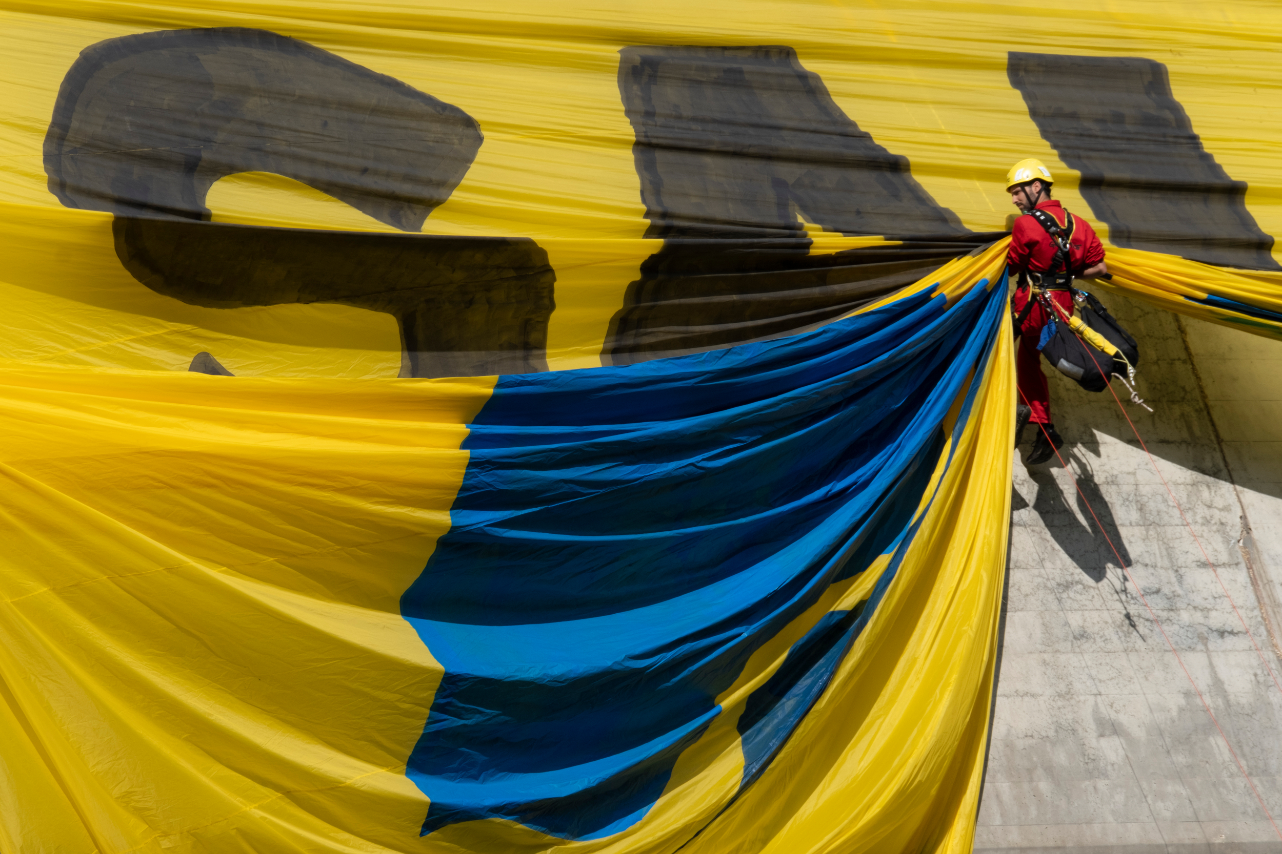 A climber unfurls an enormous yellow banner on a concrete surface