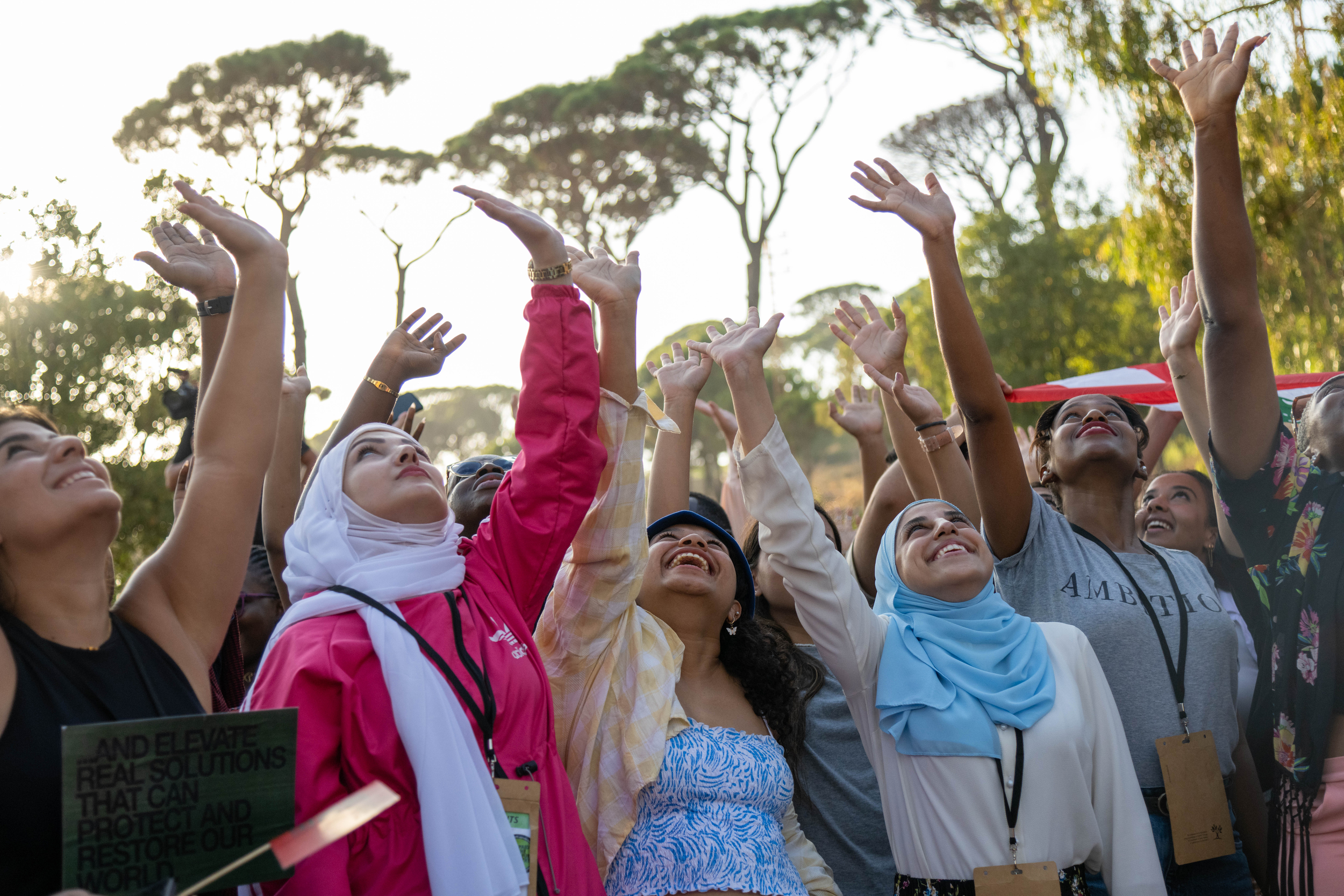 Standing together in sunshine, a group of activistshold their hands in the air and look upwards with joyful expressions.