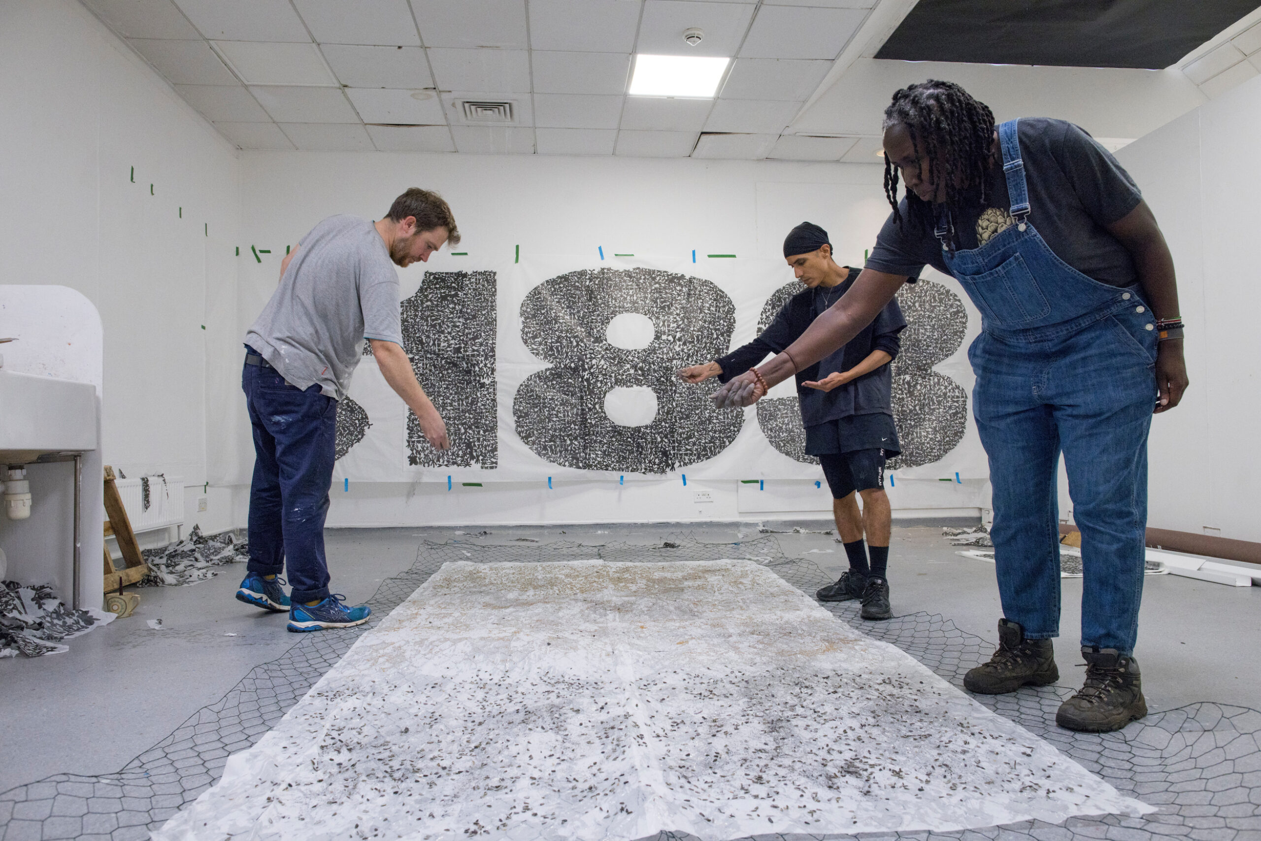 3 artists scatter seeds onto paper while making the artwork in the studio.