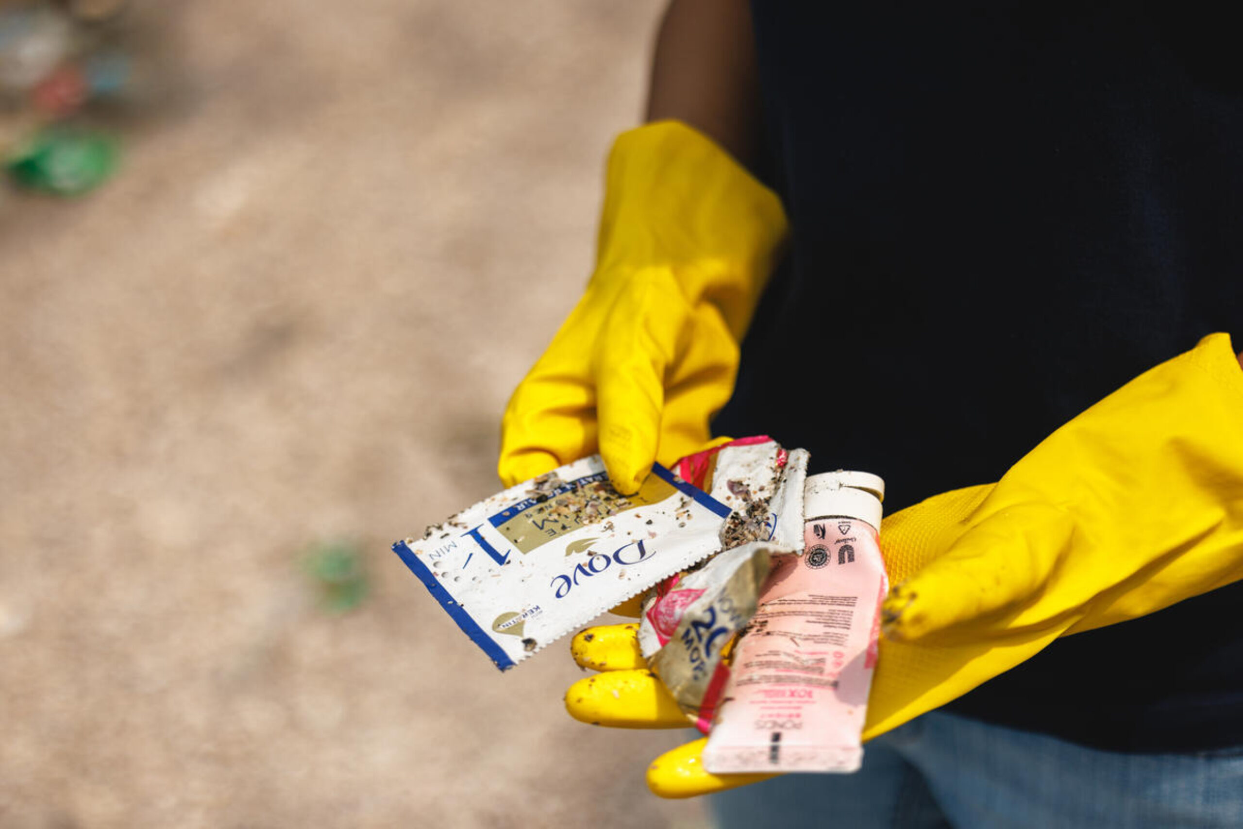 Hands wearing rubber gloves hold a range of discarded Dove branded plastic sachets.