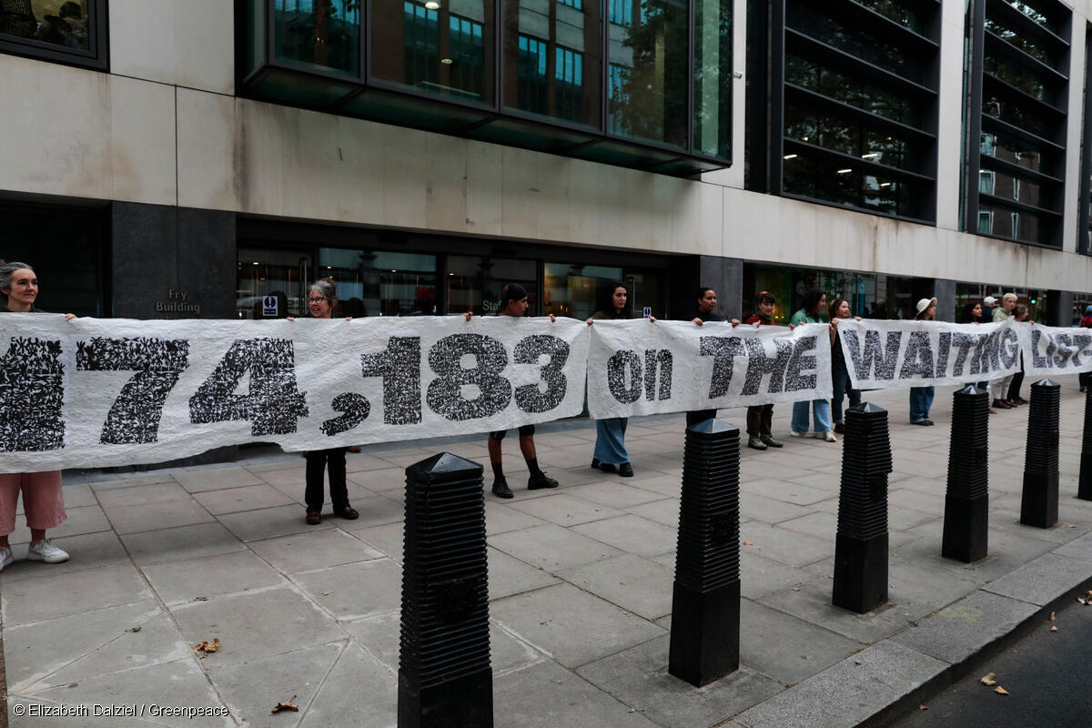 A 30 metre banner is held open by volunteers on a pavement outside an office. The banner reads 