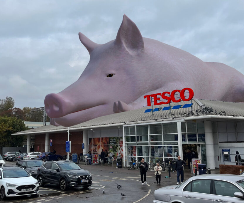 A giant digitally-rendered pig sits on top of a Tesco superstore overlooking the car park.