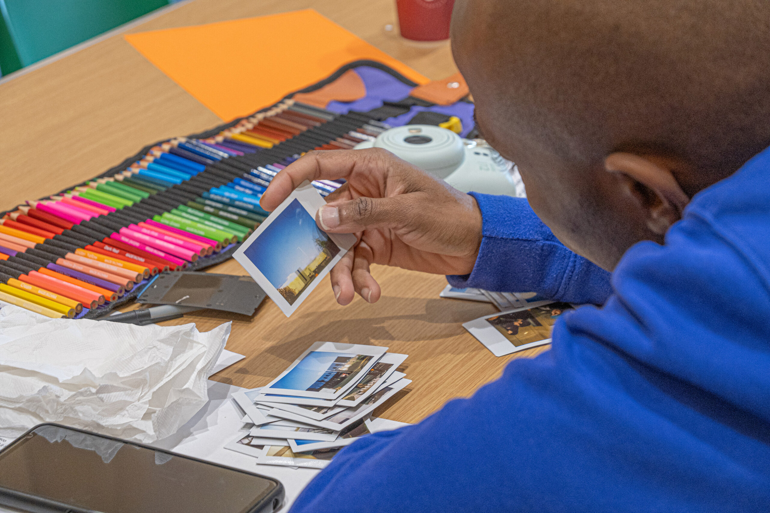 Over-shoulder picture of a Black person looking at polaroid photos on a table.