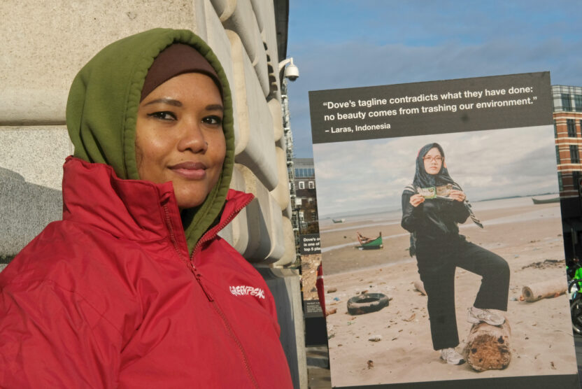 Laras Nauna, an Indonesian woman, stands in front of a large sign with a quote and photo of her criticising Dove's plastic pollution.