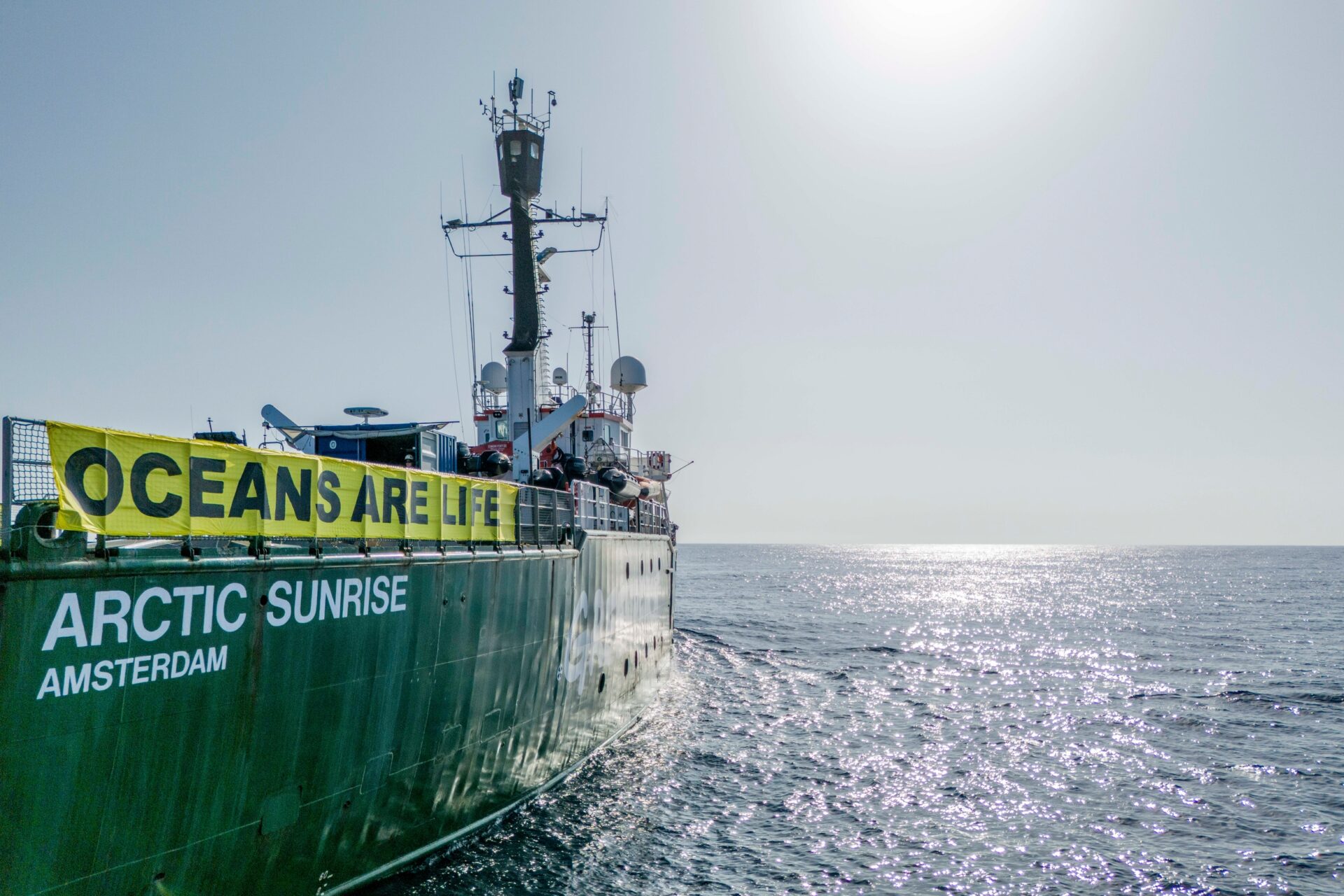 The Greenpeace ship Arctic Sunrise displays a banner reading 'oceans are life' as it sails through a calm sea.