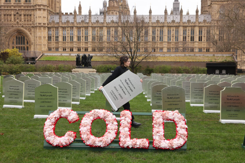 The lawn in front of the UK parliament building is covered in hundreds of mock gravestones in rows. Funeral style wording in flowers reads 'cold homes cost lives'.