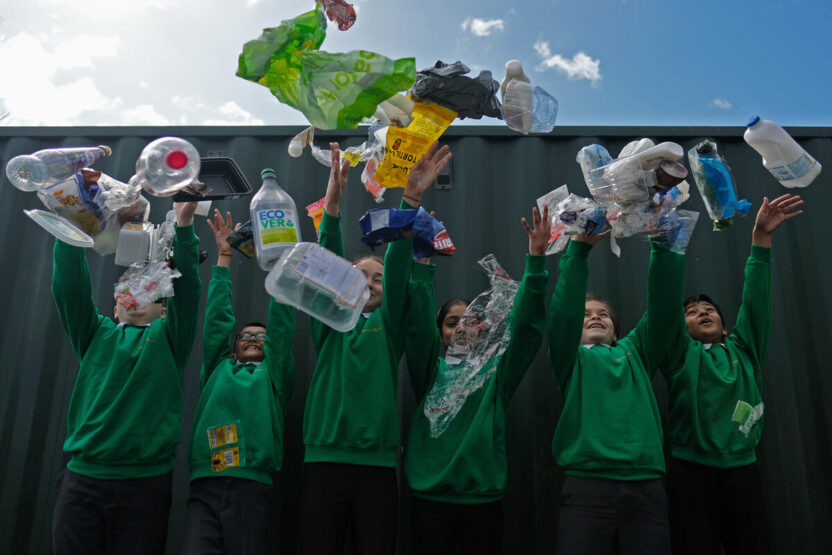 Six uniformed schoolchildren throw plastic rubbish up into the air