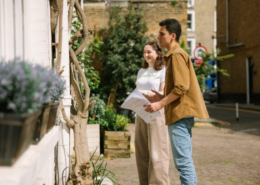 A profile of two young people standing outside a door in a nice neighbourhood on a sunny day