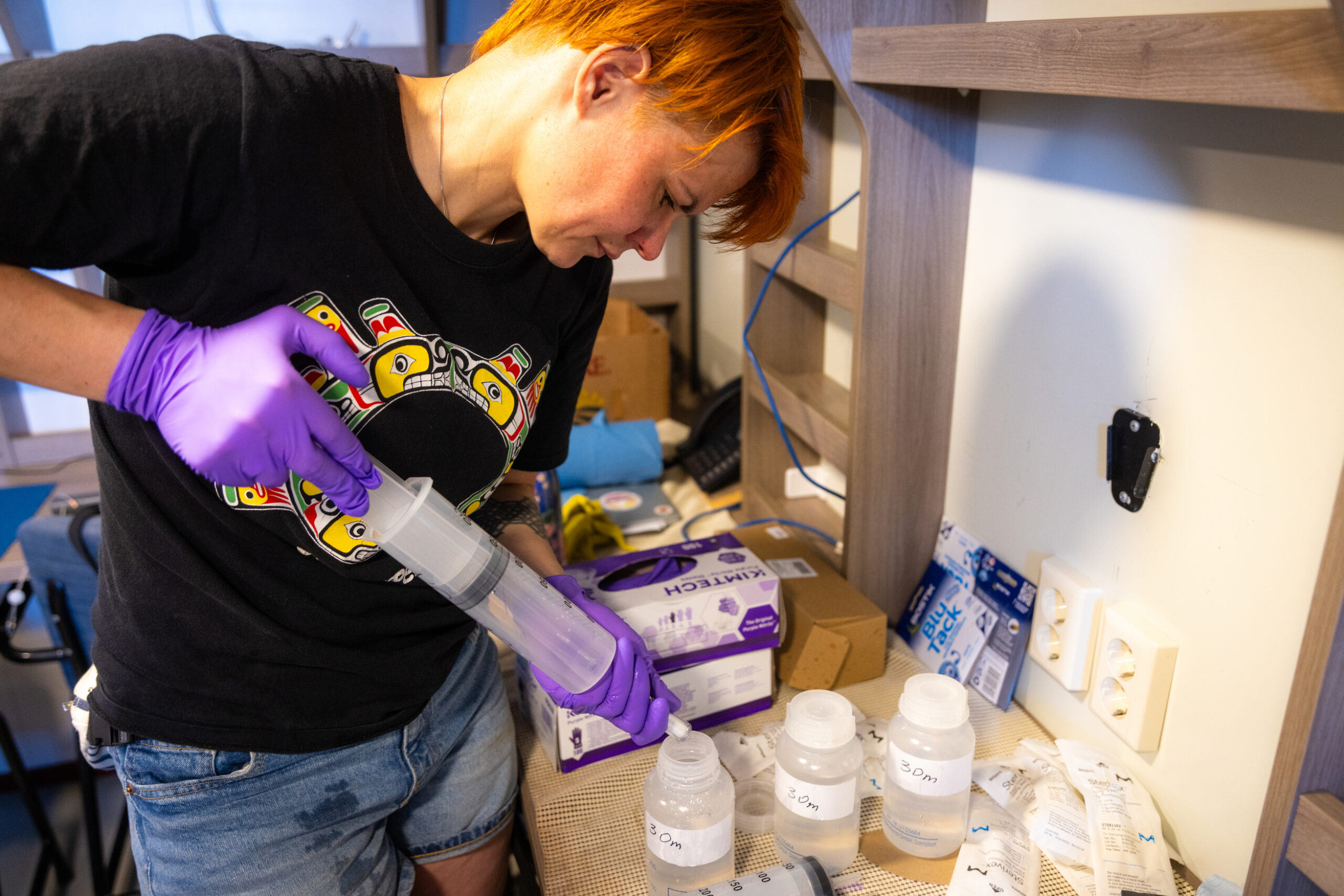 A woman pours something from a large tube into smaller containers on a countertop