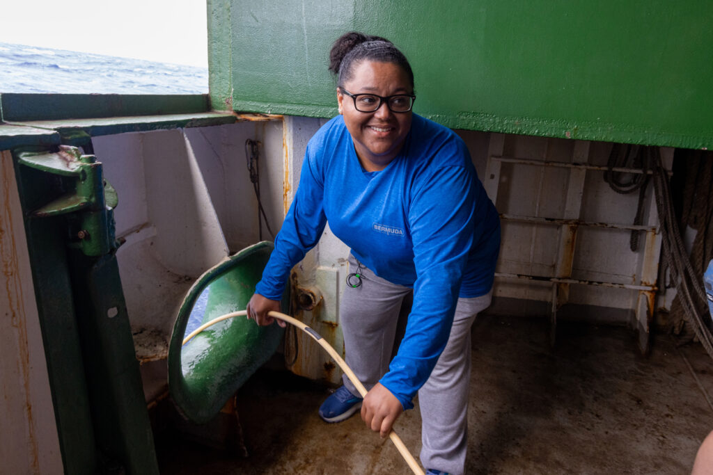 Author standing in a blue top on a lower deck of the Arctic Sunrise, feeding a cable through a hole in the ship's side