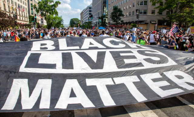 Giant black lives matter banner with a crowd of protestors in the background