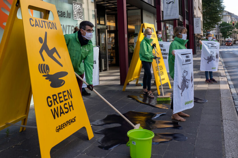 Activists dressed in green boiler suits mop the floor outside Luxembourg’s pension fund. They place yellow hazard A-board floor signs nearby that read “Caution green wash” with a symbol of someone slipping over.