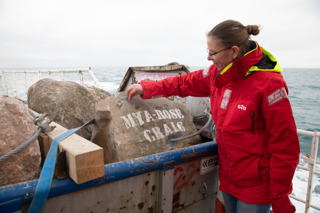 A Greenpeace crew member inspects a large boulder secured on deck, stencilled with the name Mya-Rose Craig