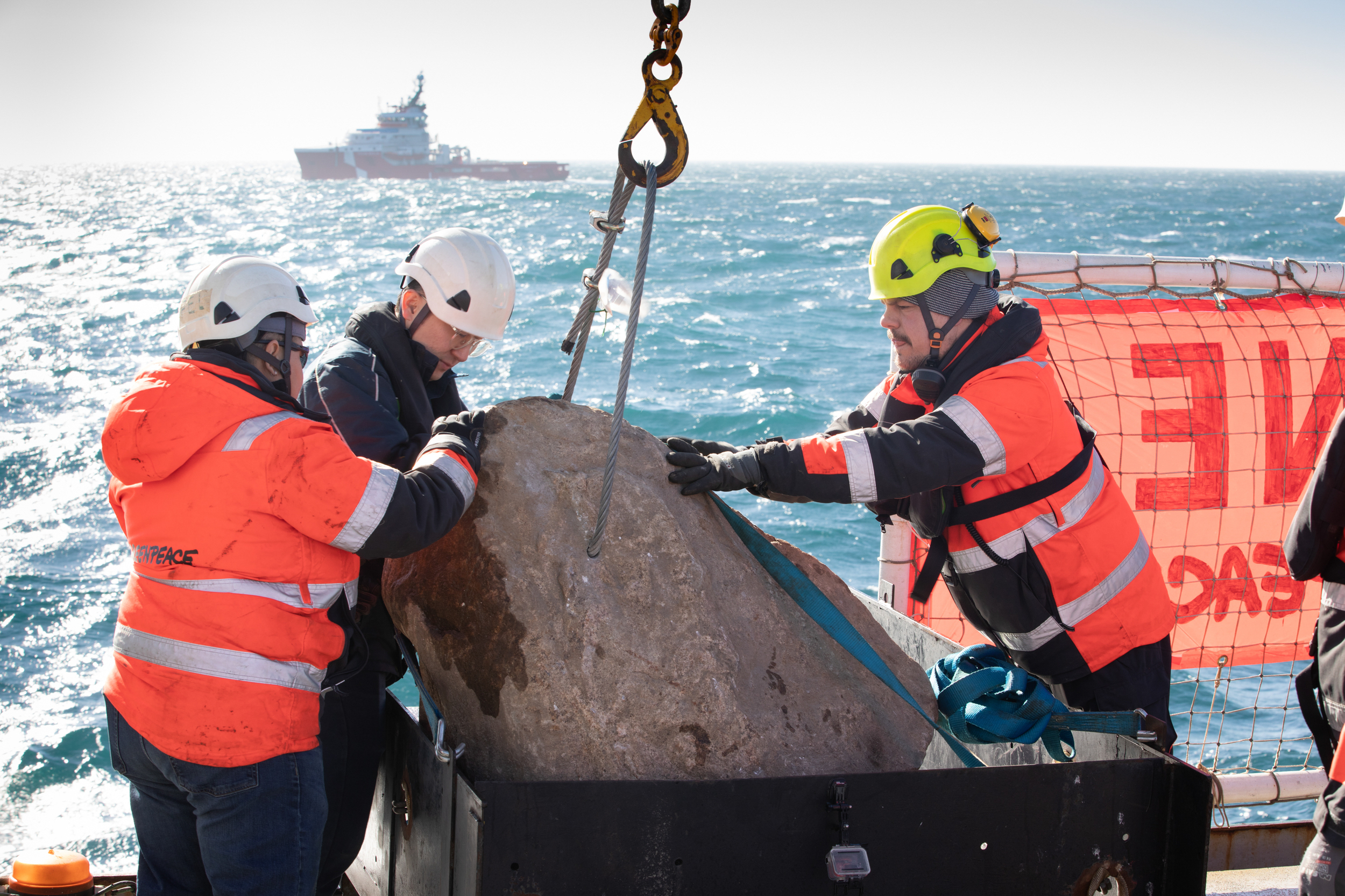 Greenpeace crewmembers prepare a boulder for placement on the seabed. A second ship is visible in the background