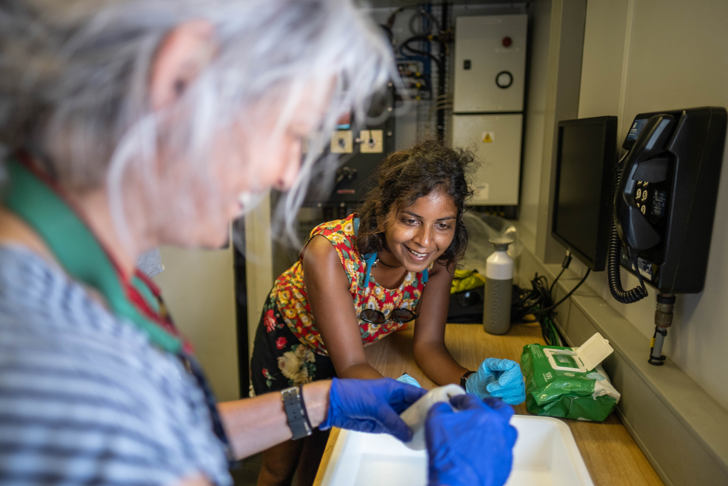 Two scientists handling samples at a work bench. One is inserting a specimen into a container, while the other looks on smilling.