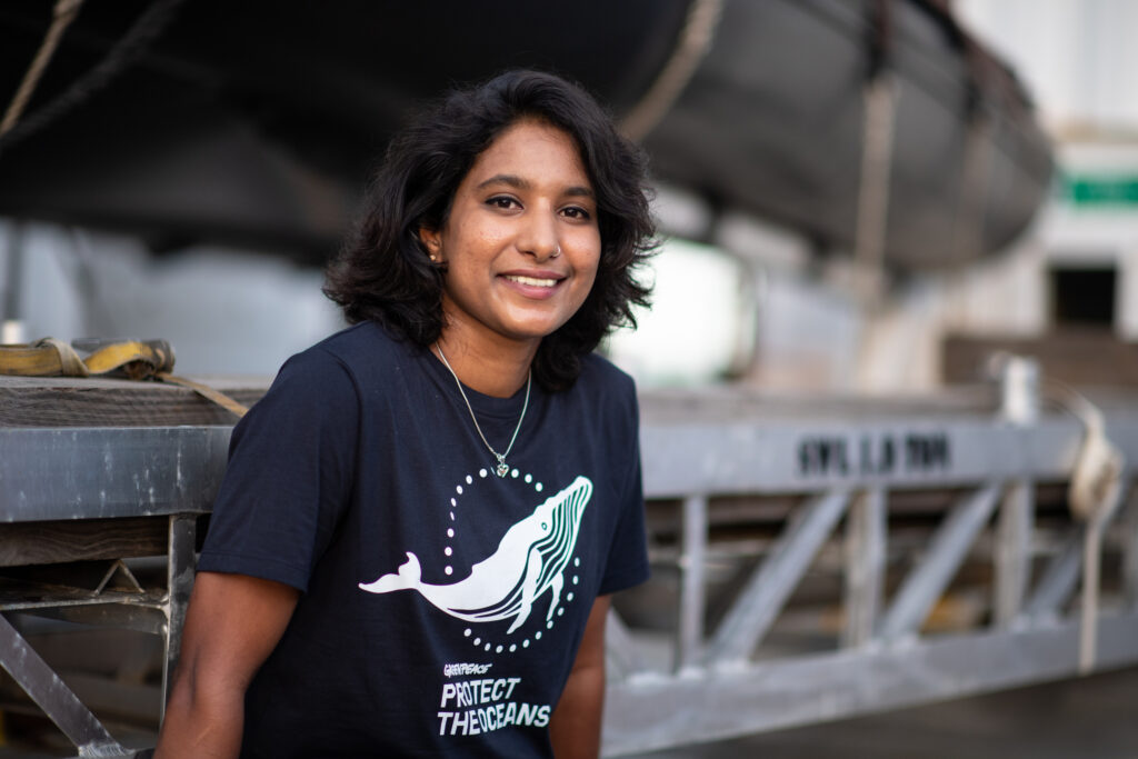 A Greenpeace crew member poses in deck wearing a protect the oceans t-shirt