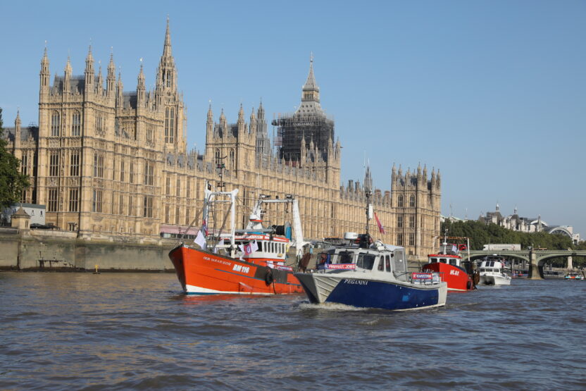 A group of small fishing boats sail alongside the UK's Houses of Parliament on the River Thames