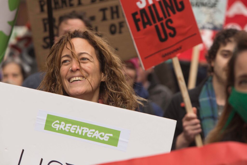 Closeup of a protester in a crowd, smiling as the wind blows their hair across their face.