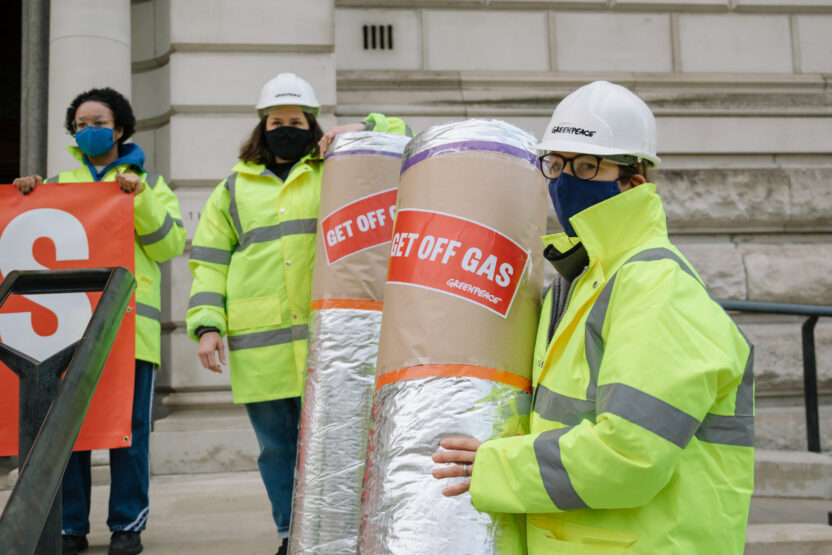 Two people in hard hats and reflective work jackets holding rolls of loft insulation, bearing labels reading 'Get off gas'