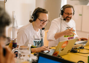 Two Greenpeace staff in matching t-shirts smile as they speak into headsets and look at laptops.