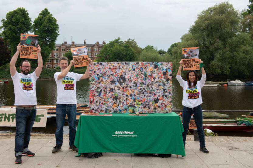 Three volunteers wearing branded tshirts stand around a street stall holding up campaign merchandise.