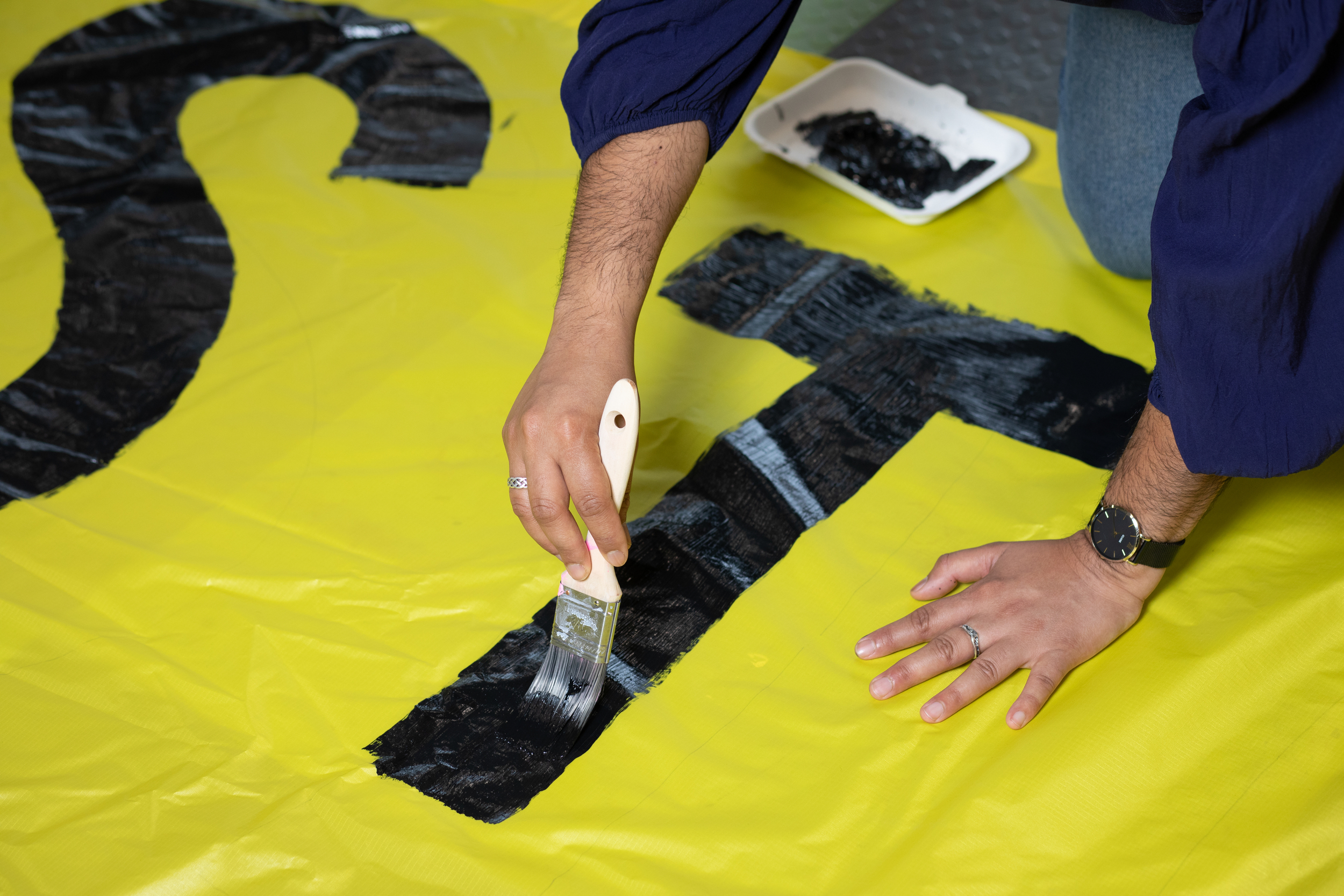 Hands painting a large black letter on a yellow banner