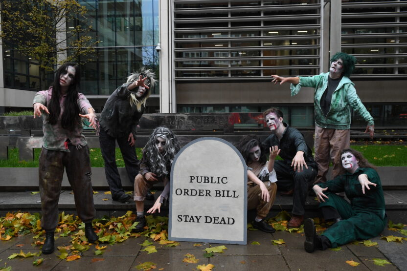 Group of people dressed as zombies with a sign in the shape of a gravestone. Text reads 