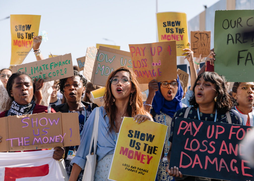 A group of protestors at a march. They hold banners with slogans including: "Pay up for loss and damage", "Show us the money" and "Stop fossil fuels"
