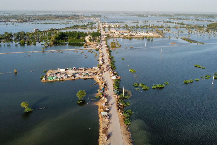 A dry road cuts through a flooded landscape. The floods stretch far into the distant horizon.