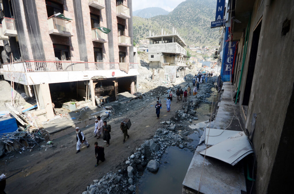 People carry food and water along a road in a destroyed town.