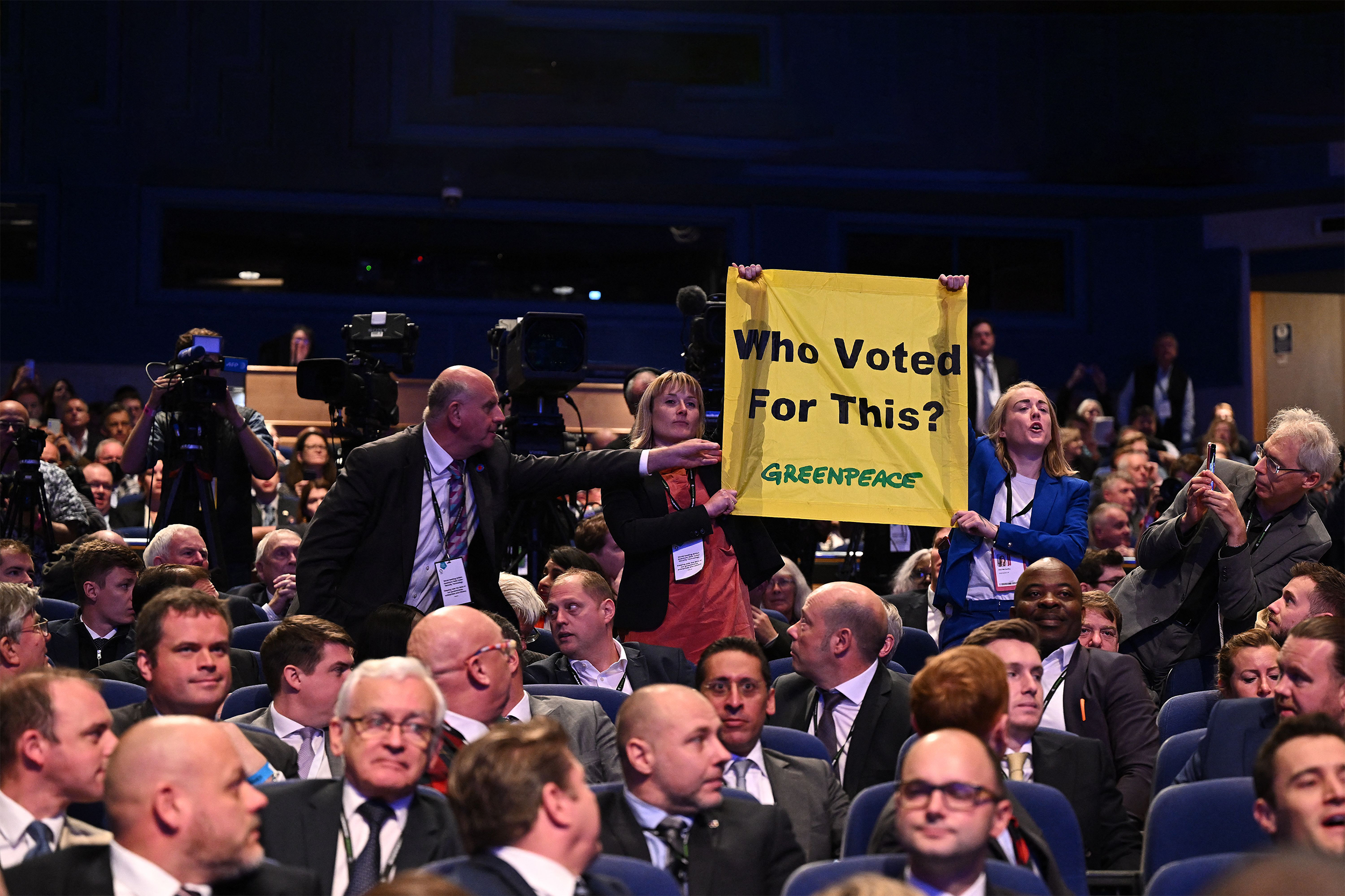 In the audience at the Conservative Party Conference, wo activists hold up a Greenpeace-branded banner reading 