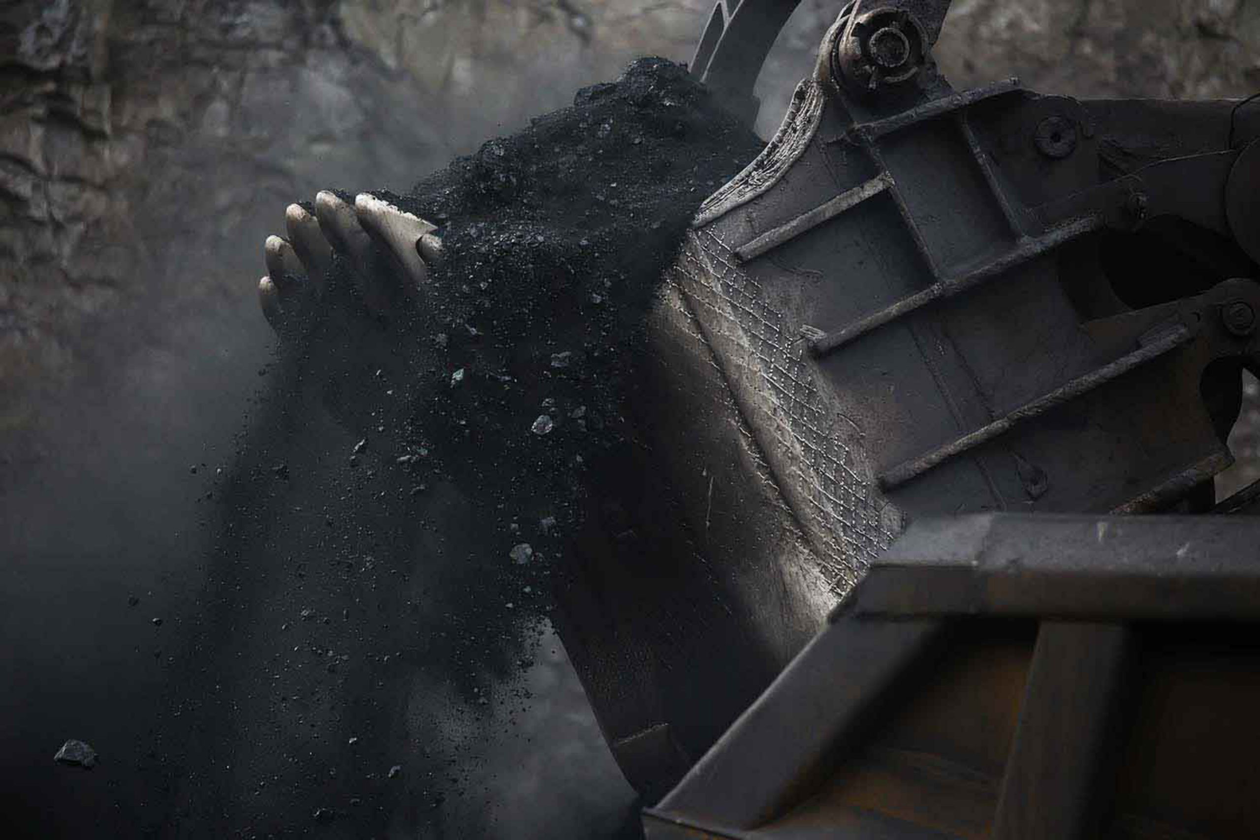 Coal fragments spill over the edge of a giant mechanical scoop as it lifts them off the ground