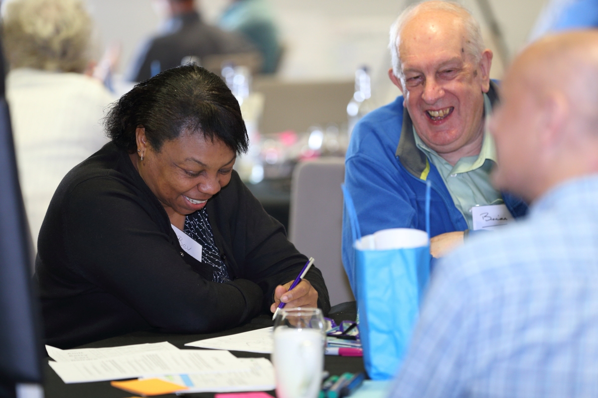 A man and a woman sit round a table smiling and laughing at the citizens climate assembly.