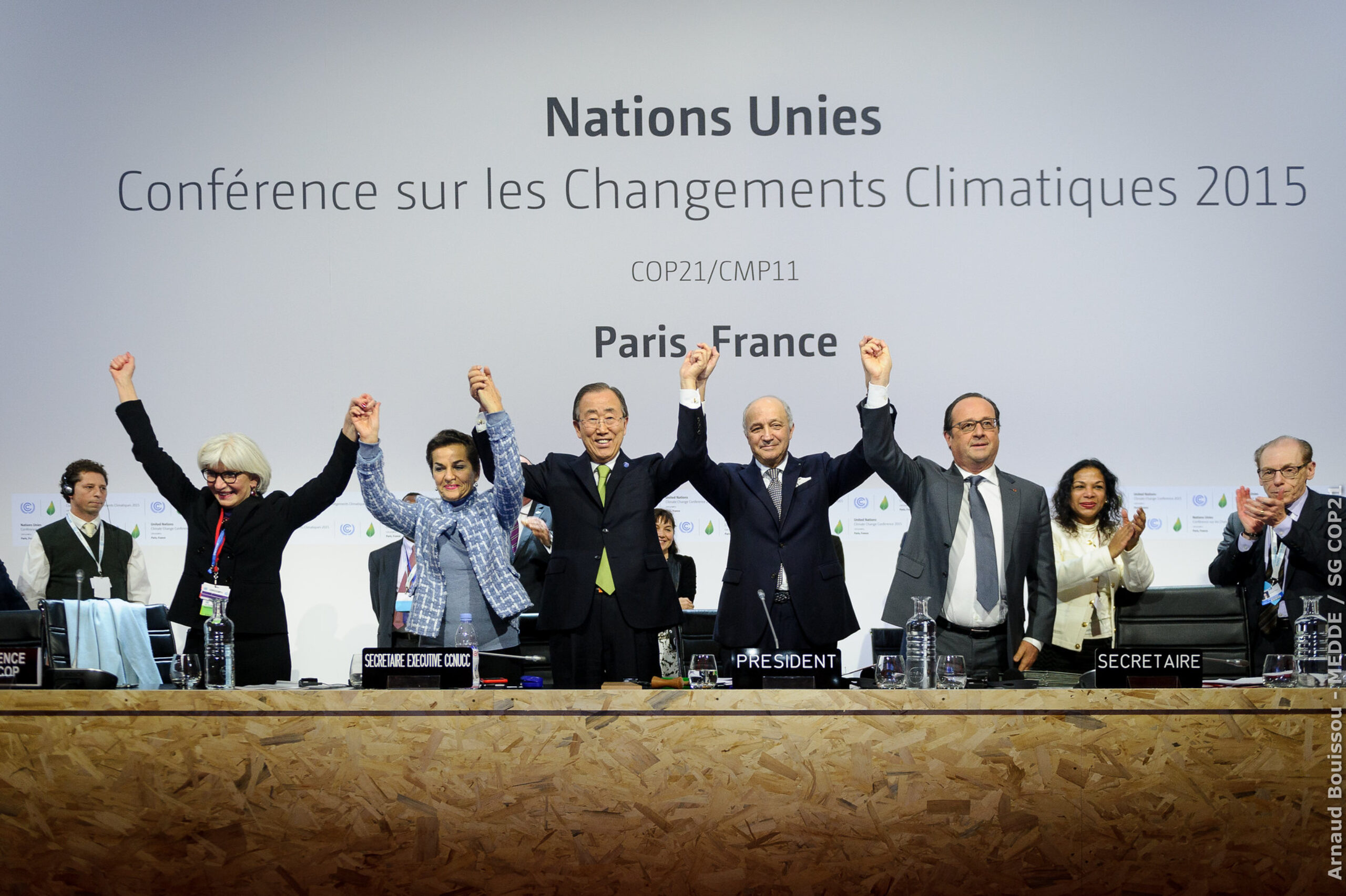 World leaders standing in a line and cheering in front of a United Nations conference backdrop during negotiations for the Paris Climate Agreement