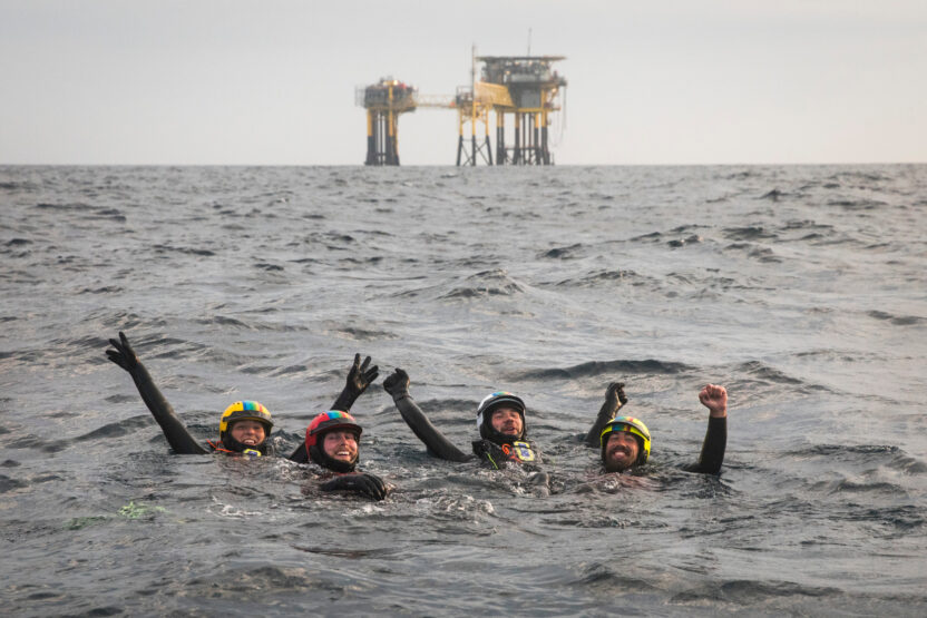 People swimming in the sea with an oil platform in the distance