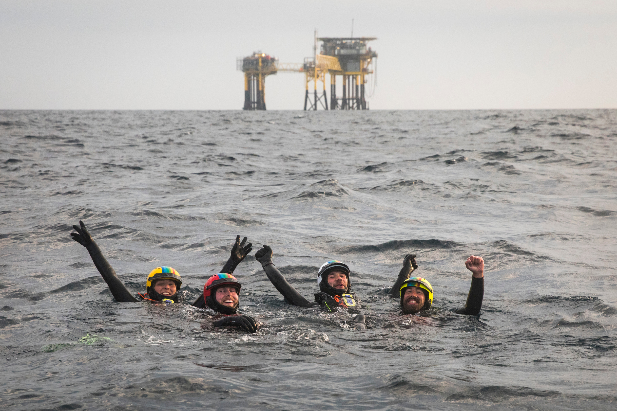 People swimming in the sea with an oil platform in the distance