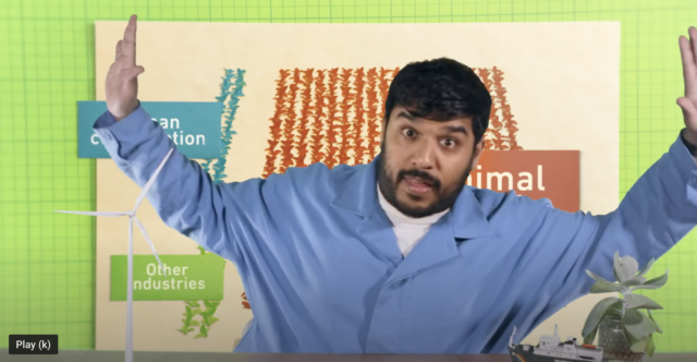 Still from a video showing a presenter gesturing in front of a diagram