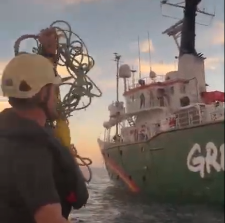 A crew member in a small boat holds up a handful of tangled rope to people on deck of a nearby Greenpeace ship